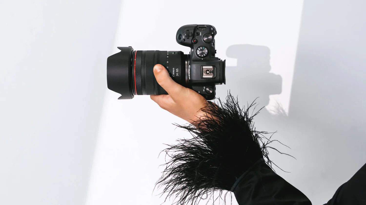 Hand holding a camera with a lens against a white background