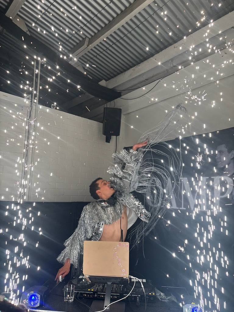 Person in silver outfit with large decorative item on stage with sparkling lights
