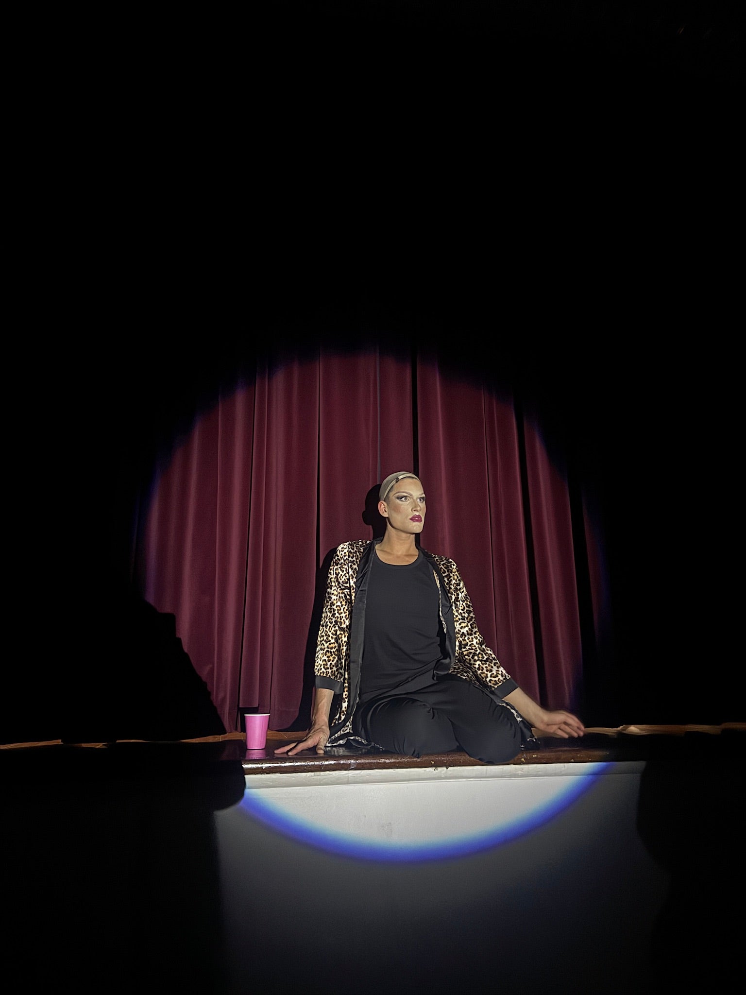 Person sitting on a stage with a spotlight, wearing a black outfit.