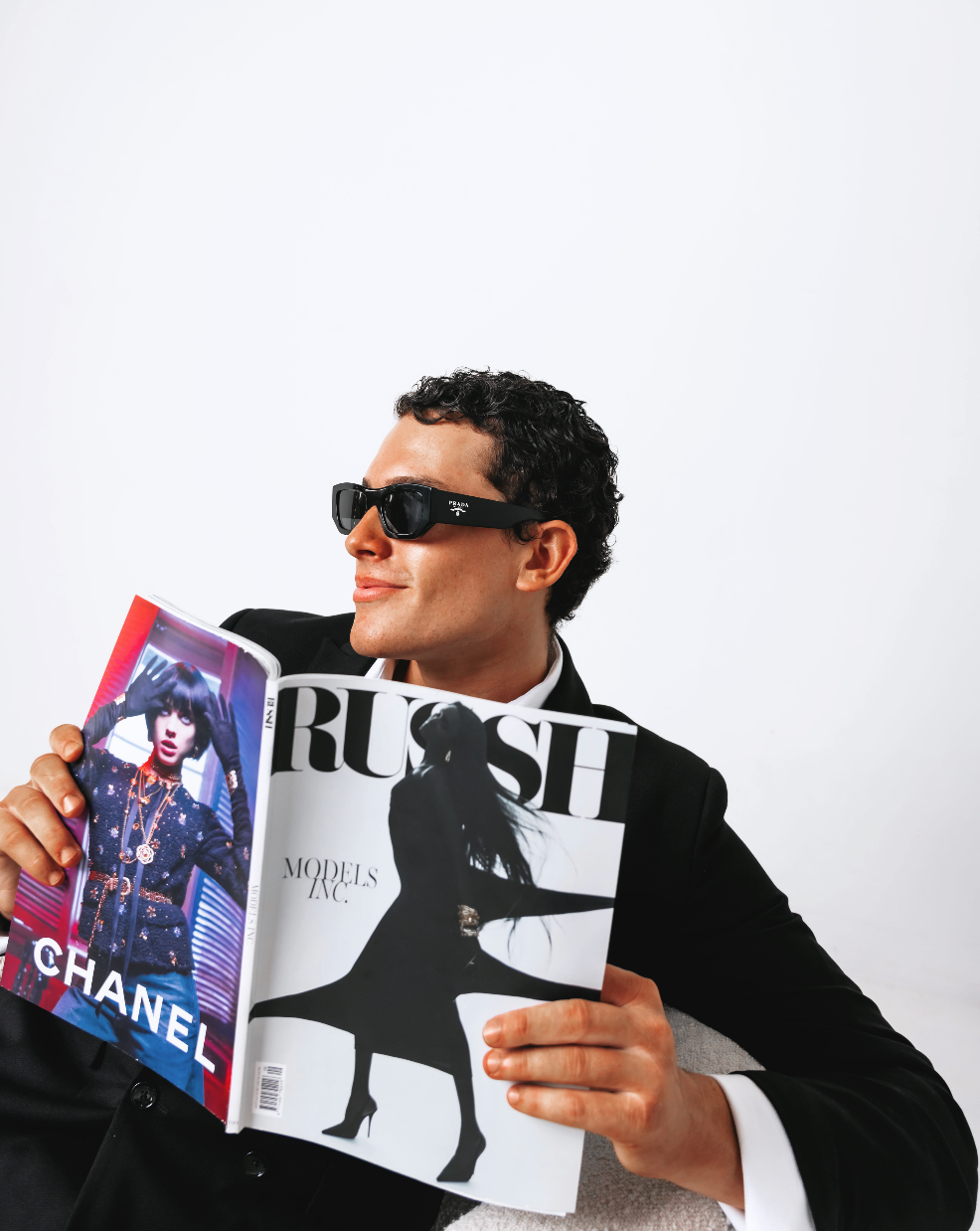 Person holding a magazine with a model on the cover, wearing sunglasses and a black suit.