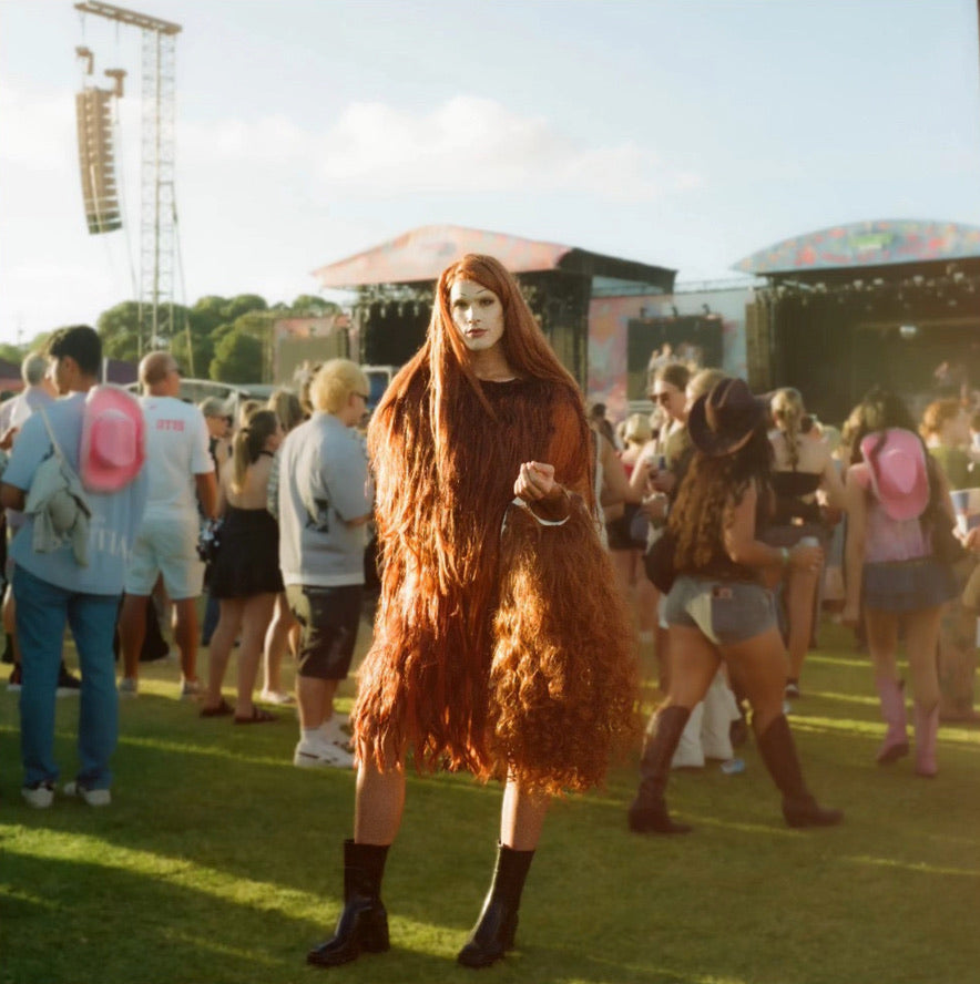 Person with long red hair wearing a brown fur coat at a music festival.